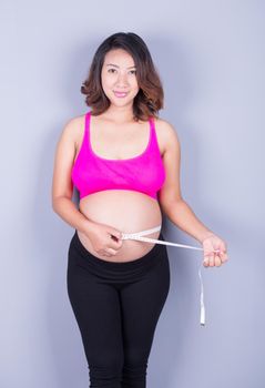 beautiful Pregnant woman with measuring tape on gray background