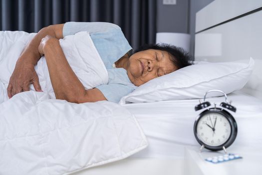 senior woman sleeping on a bed with a clock