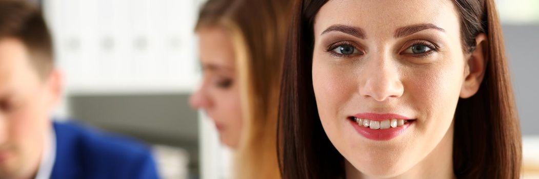 Beautiful smiling cheerful girl at workplace look in camera with colleagues group in background. White collar worker at workspace, job offer, modern lifestyle, client visit, profession train concept