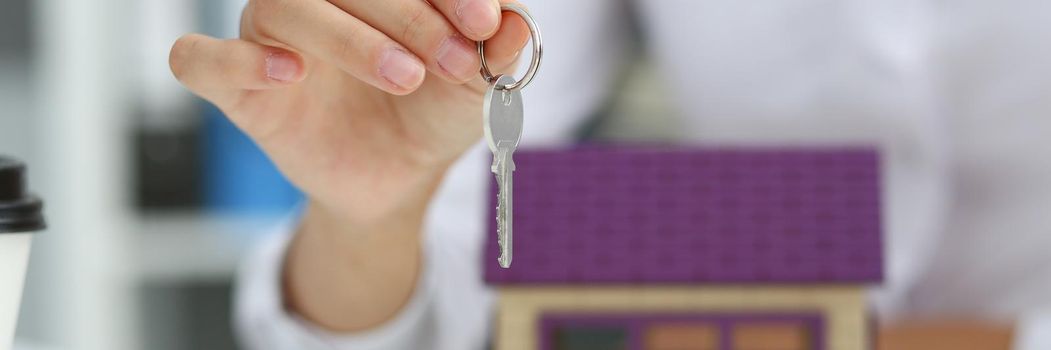 Female hand holds the key to the lock in the hand against the backdrop of the toy house sale purchase lease concept real estate services on the market