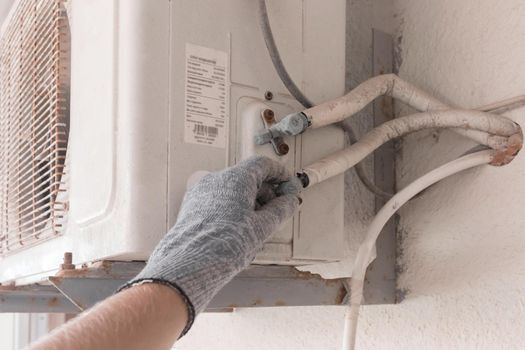 The hand of an air conditioner repair and maintenance specialist in a construction glove working with air-conditioned old equipment.