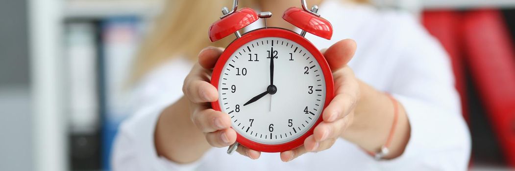 Smiling business woman holding in hand on the alarm clock a red color showing eight o'clock in the morning or evening AM PM