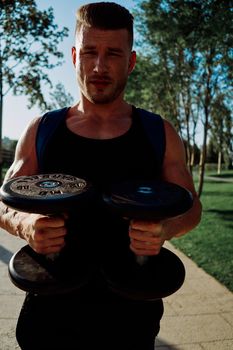 athletic man with dumbbells in his hands in the park training lifestyle. High quality photo