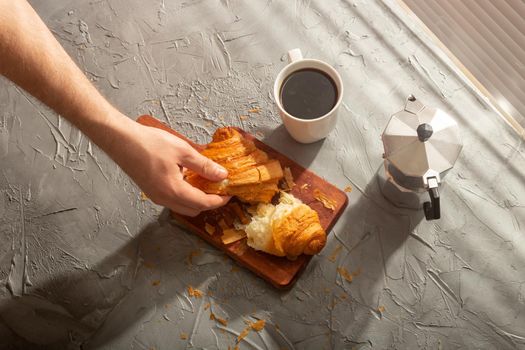 Breakfast with croissant on cutting board and black coffee. Morning meal and breakfast.