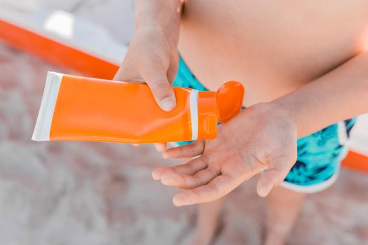 A young girl, holds sunscreen in her hands and is going to be smeared for protection from the sun against the background of the sea beach.