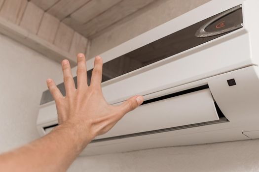 The guy puts his hand under the air conditioner in the room to check the temperature and the feeling of warm or cold air.