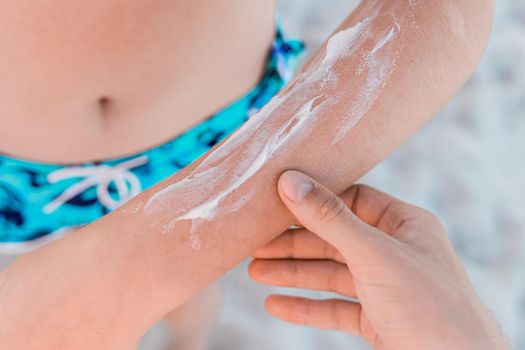 The guy's hand touches the hand of a young girl with sunscreen and sun protection against the background of the beach, close-up.