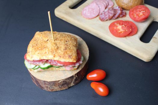 sandwich sandwich with ham sausage and vegetables cucumber tomato on a wooden stand on a black background. The serving in the restaurant is original. copyspace.