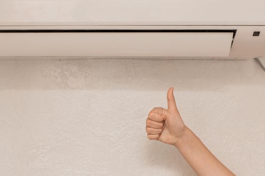 The girl's hand shows the class thumbs up under air conditioner on the wall in the room background.
