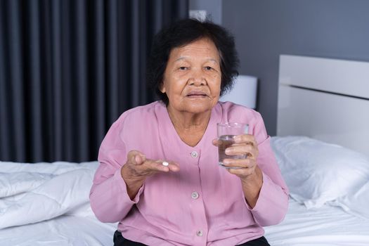 senior woman taking pill with glass of water in a bed