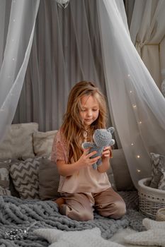 Little cute happy girl in pajamas playing with toys in a white wigwam Close up photo of a happy child