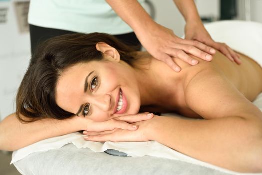 Young female receiving a relaxing back massage in a spa center. Brunette woman patient is receiving treatment by professional therapist.