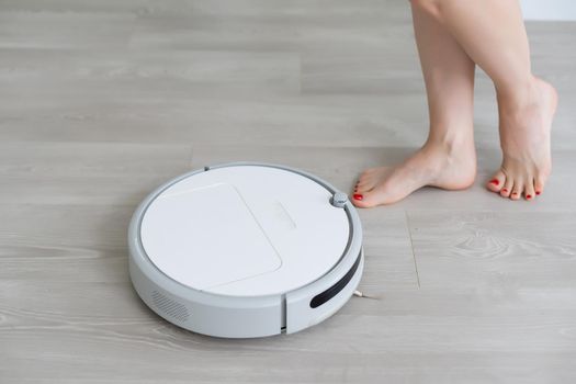 Woman using robotic vacuum cleaner at home.Female legs near robot cleaner