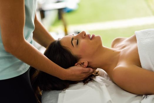 Young caucasian smiling woman receiving a head massage in a spa center with eyes closed. Female patient is receiving treatment by professional therapist.