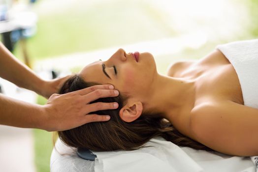 Young caucasian smiling woman receiving a head massage in a spa center with eyes closed. Female patient is receiving treatment by professional therapist.