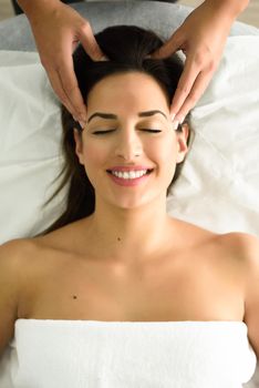 Top view of young caucasian smiling woman receiving a head massage in a spa center with eyes closed. Female patient is receiving treatment by professional therapist.