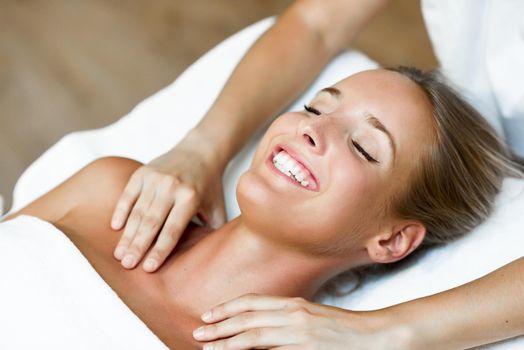 Young blond woman receiving a head massage in a spa center with eyes closed and smiling. Female patient is receiving treatment by professional therapist.