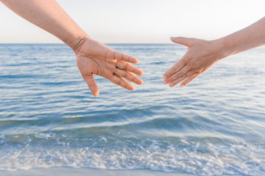 The man's hand reaches for the woman's hand against the background of the sea. Romantic Relationships and Friendship Concept.