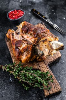 Roasted pork knuckle eisbein on a wooden board with herbs. Black background. Top view.