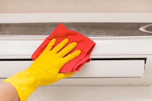 The hand of a man in a red household glove wipes and cleans the air conditioner. Maintenance and cleaning indoor service.