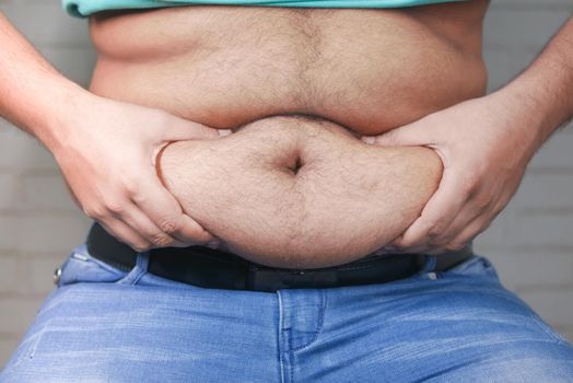 man's hand holding excessive belly fat, overweight concept.