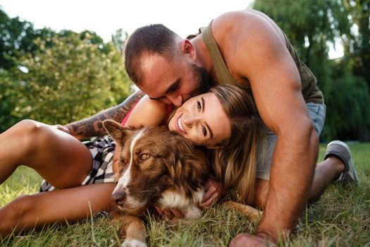 Young happy couple playing with their dog smiling in park, close up