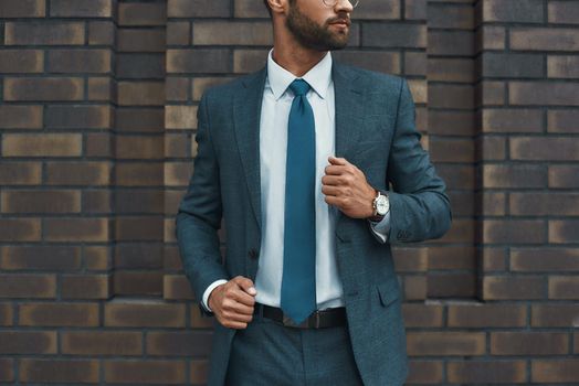 Cropped photo of a businessman in full suit standing against brick wall. Business concept. Stylish people