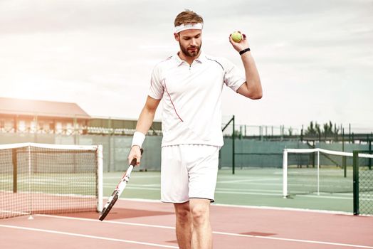 Tennis player in white sportswear with the racket and the ball in his hands is going to play tennis