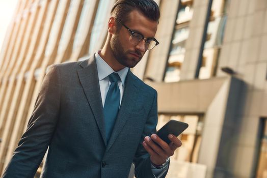 Important message. Portrait of handsome bearded businessman in formal wear using smart phone while walking outdoors. Business concept. Digital concept