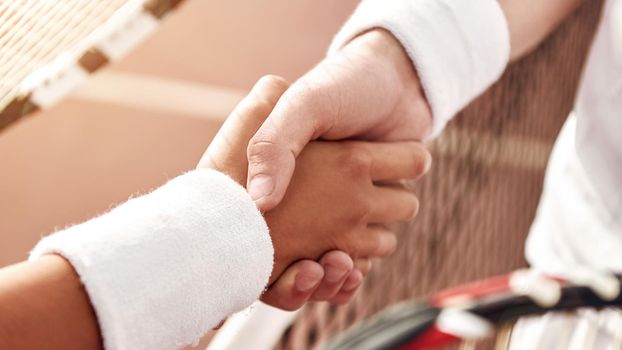 Shaking hands after good game. Close-up of man and woman in wristband shaking hands upon the tennis net