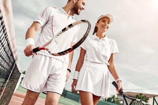 Beautiful couple walking on the tennis court with smile. Horizontal shot