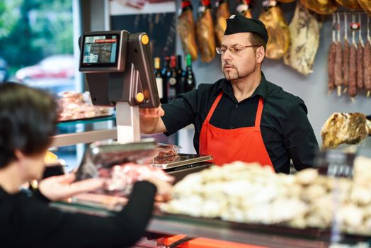 Butcher attending a customer in a butcher's shop weighing the meat and charging