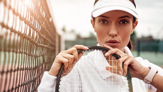 Beautiful sportswoman sitting with a racket on a court, looking at camera. Healthy lifestyle. Horizontal shot