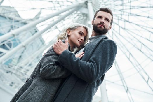 Romantic date outdoors. Young couple standing at entertainment park hugging looking aside pensive bottom view close-up