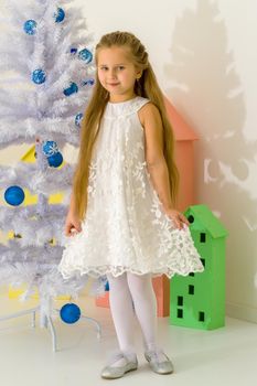 Beautiful little girl near the Christmas tree. The concept of family holidays, children's emotions.