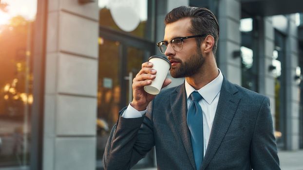 Confident and successful. Young businessman in formal wear drinking coffee and looking away while standing outdoors. Business concept