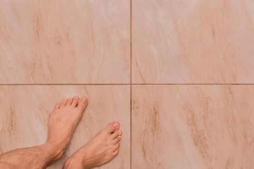 Bare feet man barefoot stands on the tile floor background, top view.