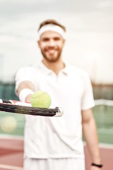 Portrait of male tennis player. Front view. Selective focus on a ball lying on the racket. Vertical shot