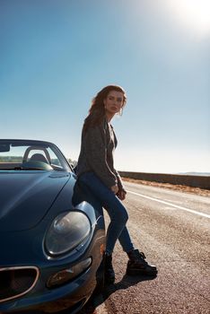 Young woman near roofless car outdoors on sunny day near the empty road. No people, sportive black car