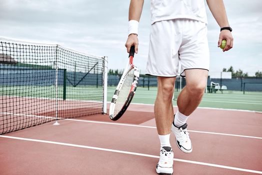 Close up male feet with tennis rocket on court. He keeping racket while playing tennis