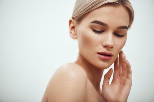 I love my skin. Attractive young blonde woman keeping eyes closed and touching her face while standing against grey background. Skin care. Beauty concept