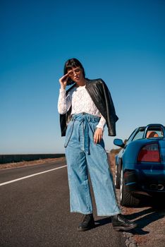 Young woman near roofless car and smiling outdoors on sunny day near the empty road. No people, sportive blue car