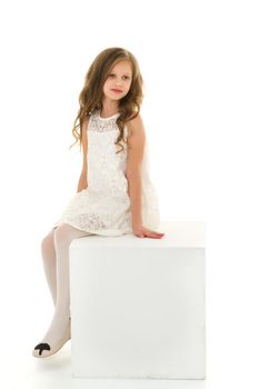 Beautiful Preteen Girl in White Dress Sitting on Cube, Portrait of Cheerful Blonde Long Haired Girl Wearing Elegant Stylish Clothes Posing in Studio on Isolated White Background