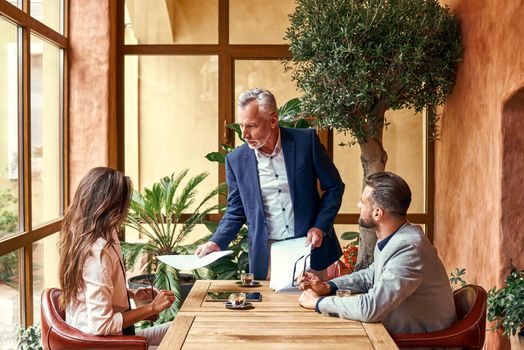 Business lunch. Three people in the restaurant sitting at table boss giving documents to employees serious. Team work concept