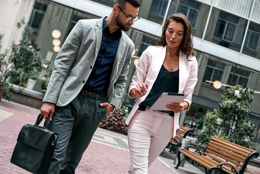 Creative ideas. Two young business people walking outside on the city street woman showing project on digital tablet to boss