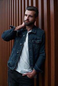 Freestyle. Young man standing leaning on wooden wall isolated touching neck looking aside pensive