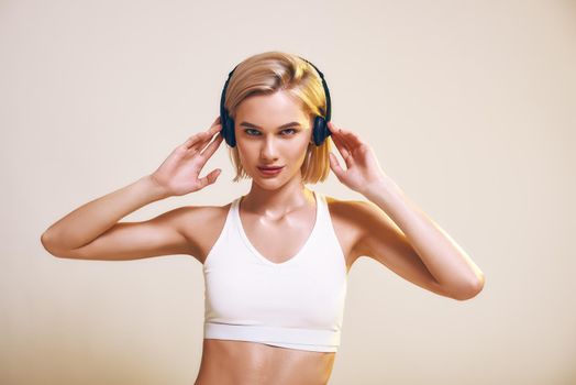 Love this music. Cute and sporty woman adjusting headphones and looking at camera while standing against pink background. Sport. Music concept