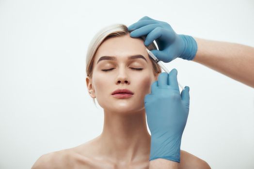 Cosmetic injection. Portrait of young pretty woman keeping eyes closed while doctors hand in blue medical gloves making an injection of botox in her face. Beauty. Facial surgery