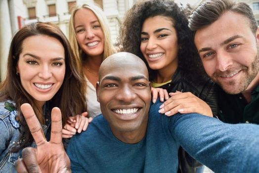 Multiracial group of friends taking selfie in a urban street with a black man in foreground. Three young women and two men wearing casual clothes.