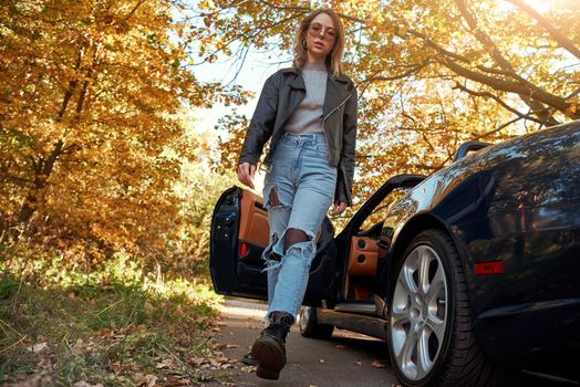 Beautiful girl near the roofless car. Autumn season, leather coat and jeans, stylish sunglasses on head